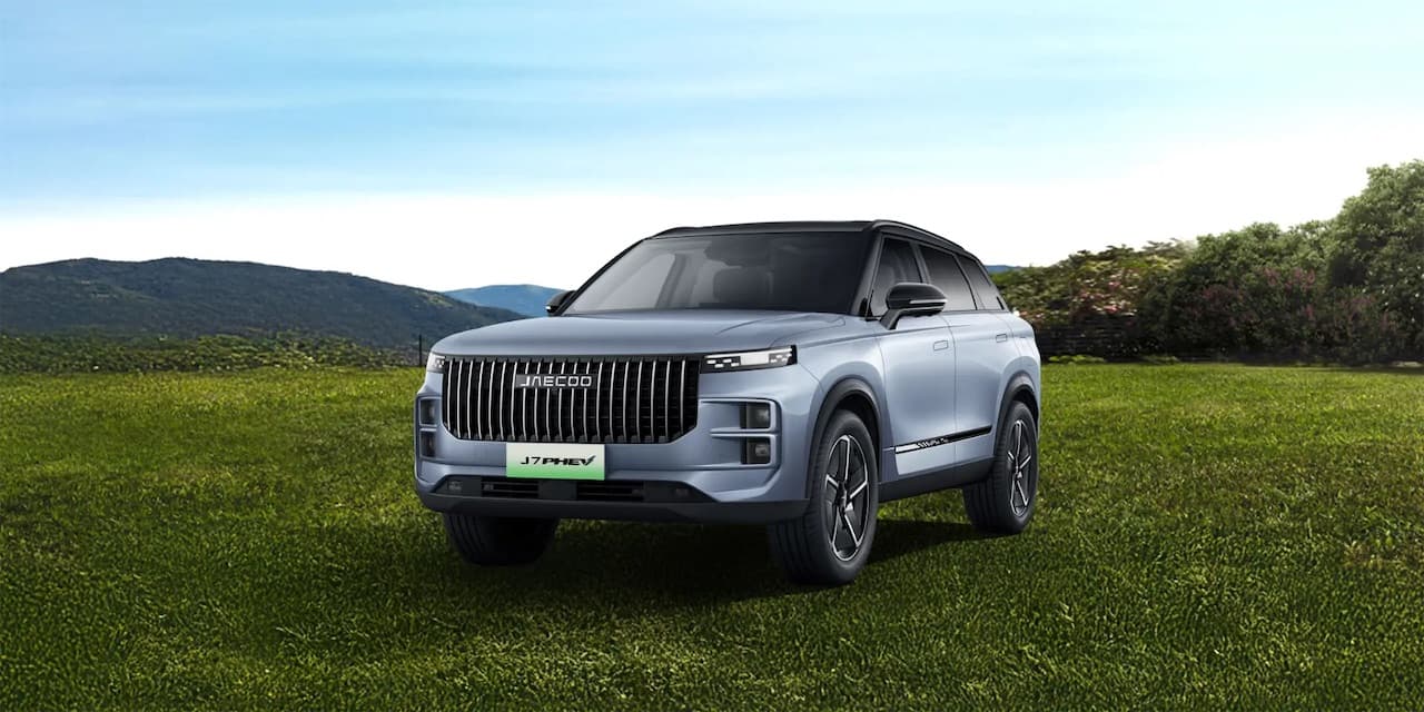 Jaecoo J7 PHEV parked on a meadow with hills behind